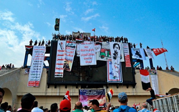 In this Oct. 30, 2019, photo, Iraqi anti-government protesters hang their demands and slogans while standing on a building near Tahrir Square, Baghdad, Iraq. An abandoned building in central Baghdad has emerged as the epicenter of anti-government protests in Iraq, with hundreds holed up inside. The Saddam Hussein-era building known as the “Turkish Restaurant” overlooks Tahrir Square, the Tigris River and the Green Zone, and protesters who took it over on Oct. 25 have sworn not to leave it. (AP Photo/Hadi Mizban)